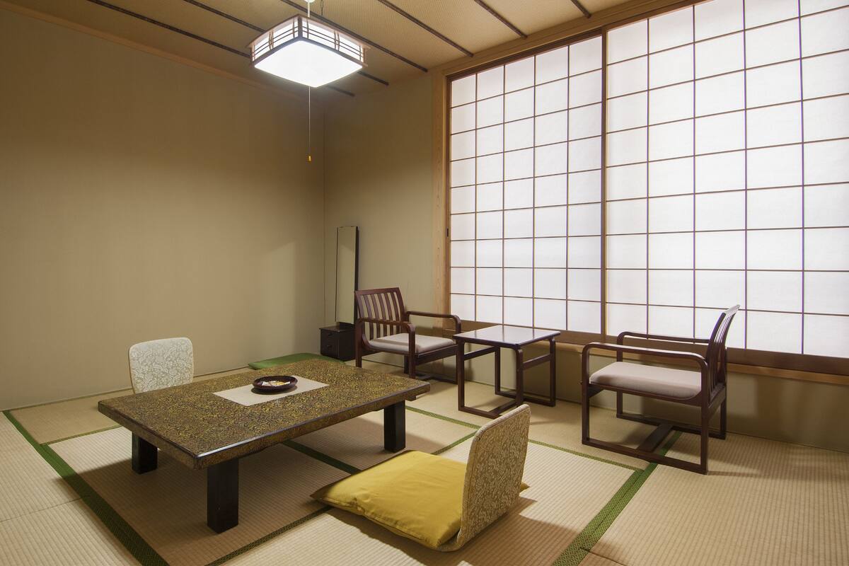 Ein traditioneller japanischer Raum mit Tatami-Böden, einem niedrigen Tisch, zwei Stühlen und einer Schiebetür.