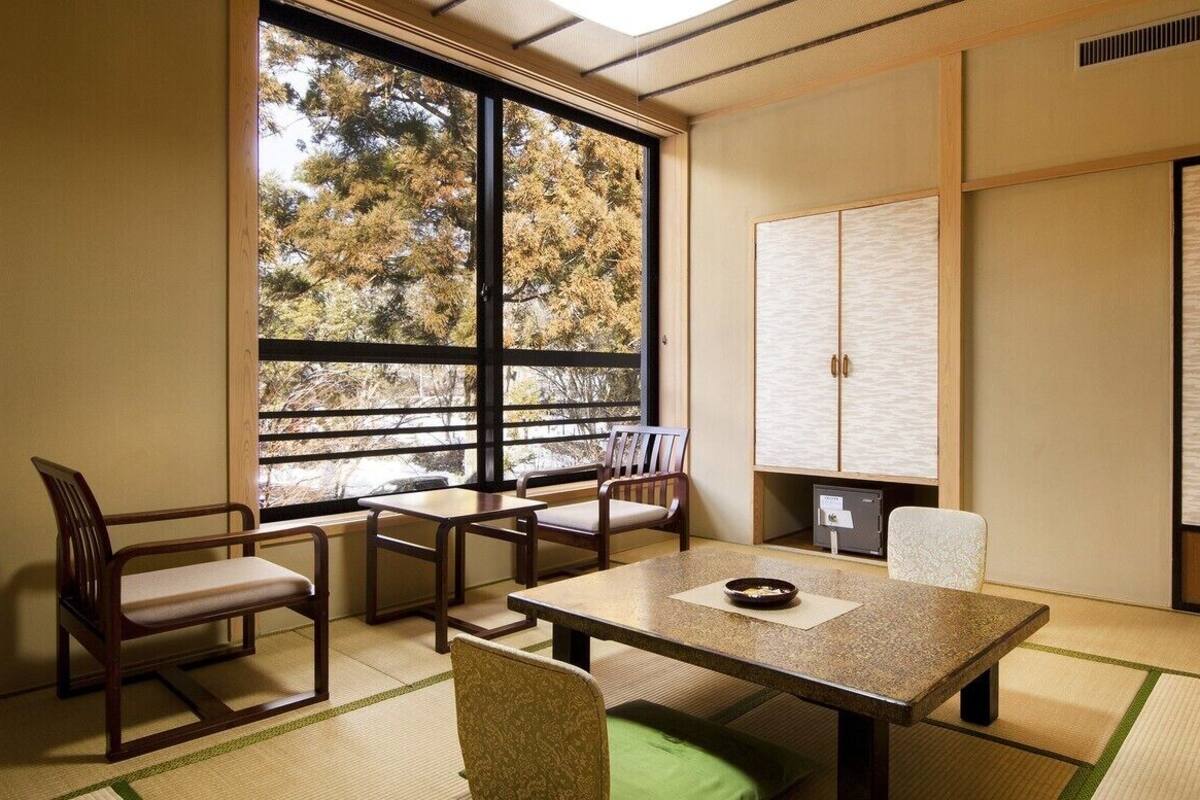 Ein traditioneller japanischer Raum mit Tatami-Bodenbelag, einem niedrigen Tisch, Stühlen und Schiebetüren.
