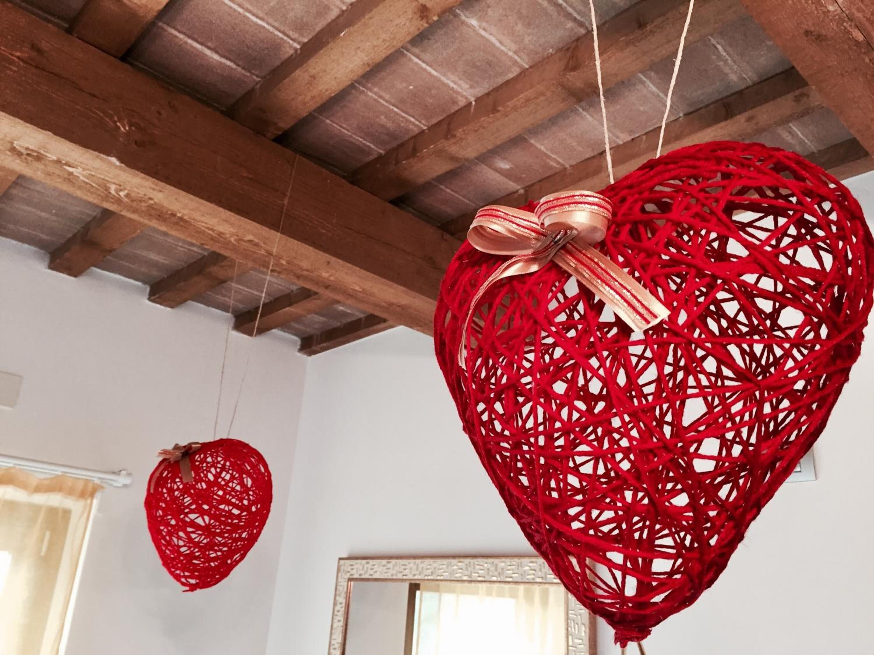 Una habitación con vigas de madera en el techo, un espejo grande y dos adornos con forma de corazón rojo.