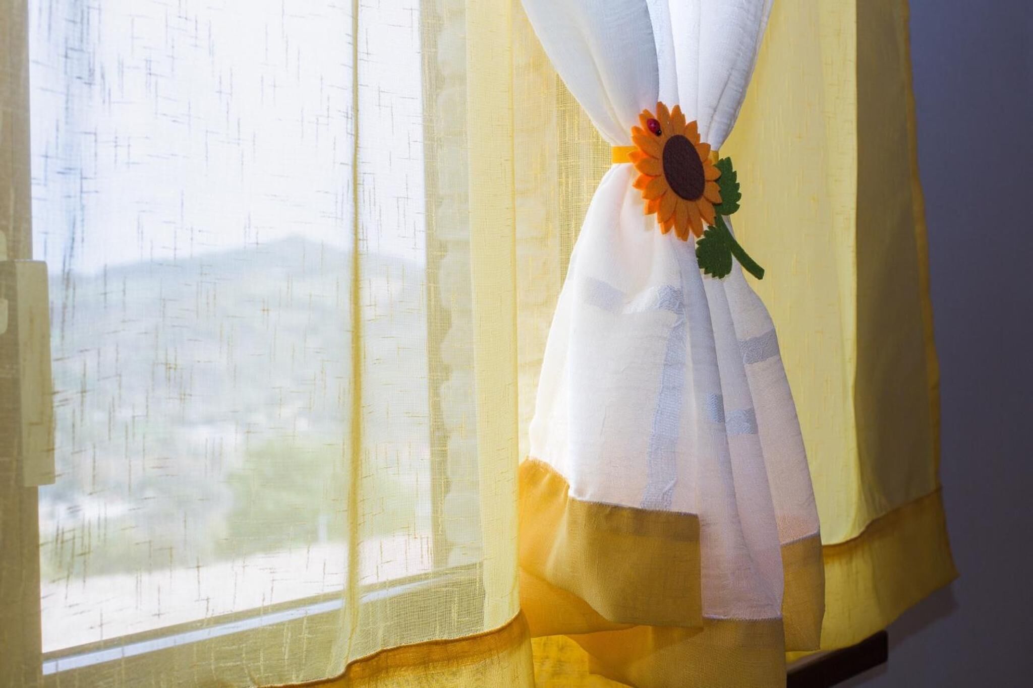 Uma janela com cortinas finas e um objeto decorativo com um girassol.