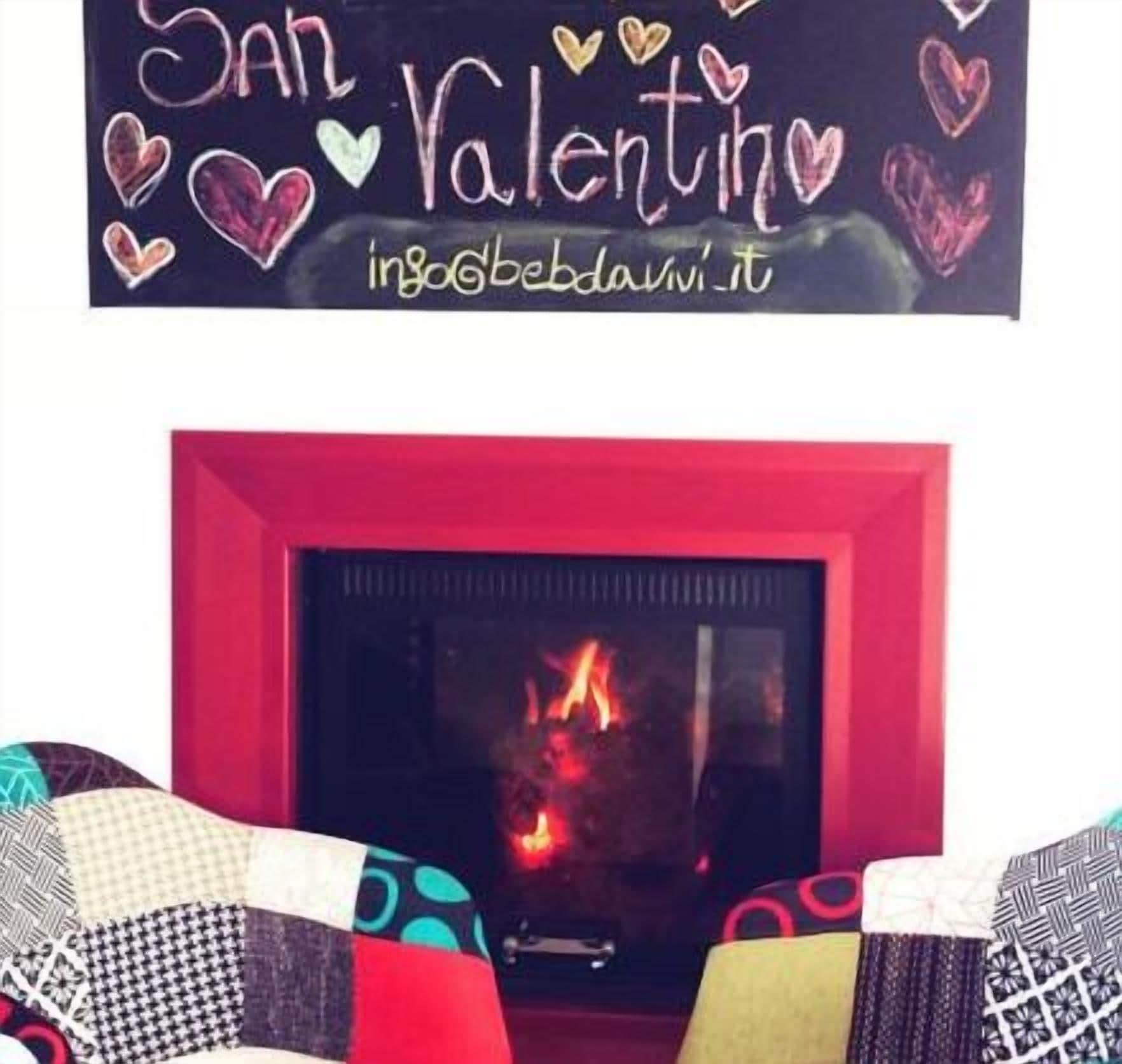 A fireplace with a red frame and a sign above it that reads "San Valentino" with hearts and the website "inbaobedawi.it".