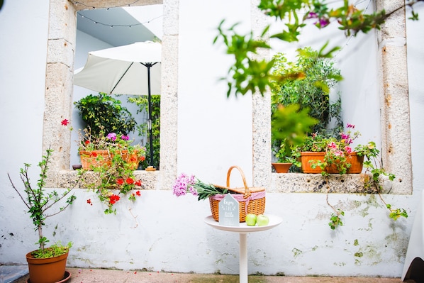 A small table with a basket and a sign, surrounded by potted plants and flowers.