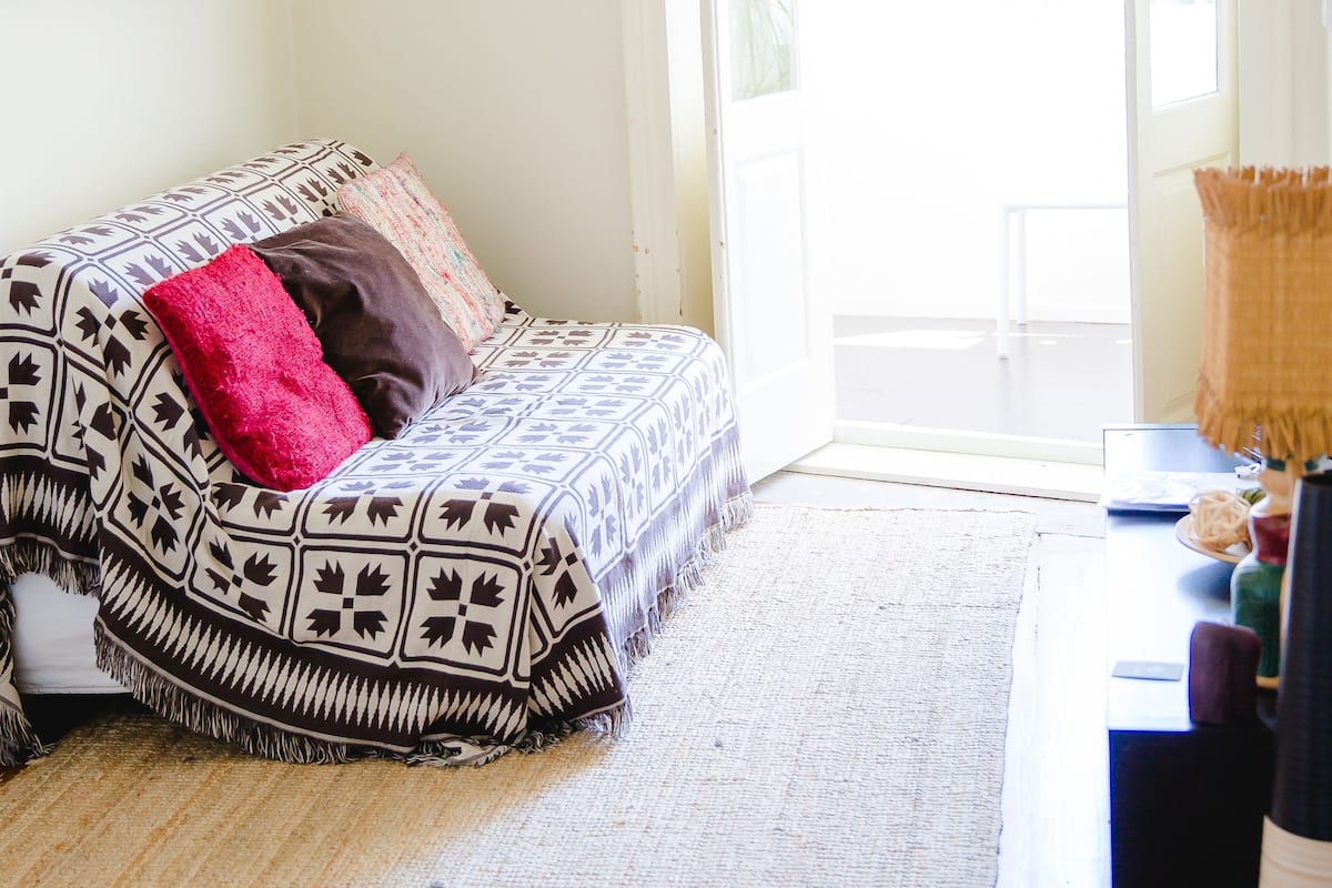 A room with a bed, a rug, a wooden floor, and a door leading outside.