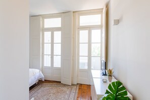 Une chambre à coucher avec un lit, une grande fenêtre, un bureau avec une plante et une porte.