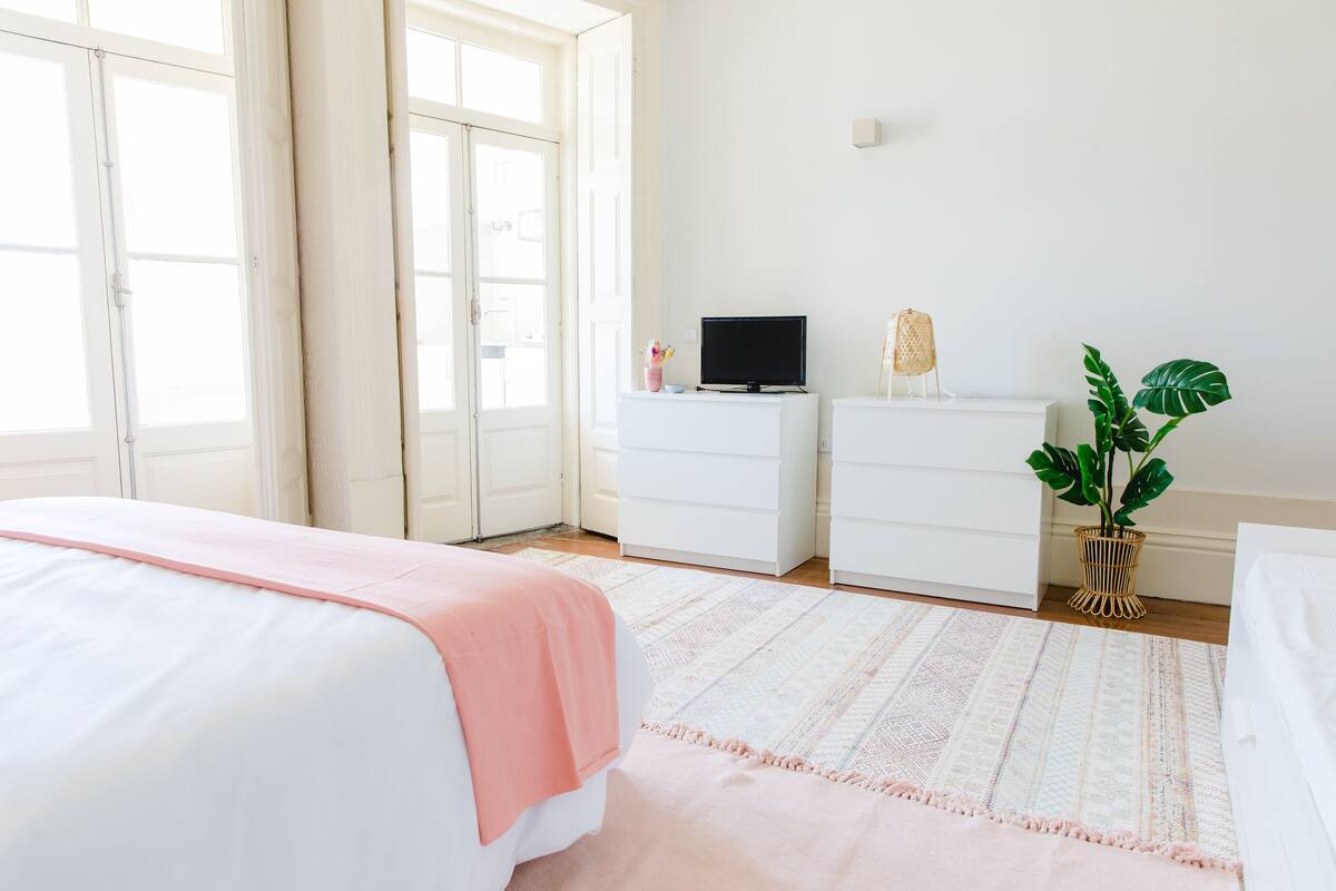 A bedroom with a bed, a TV on a dresser, a plant, and a window.