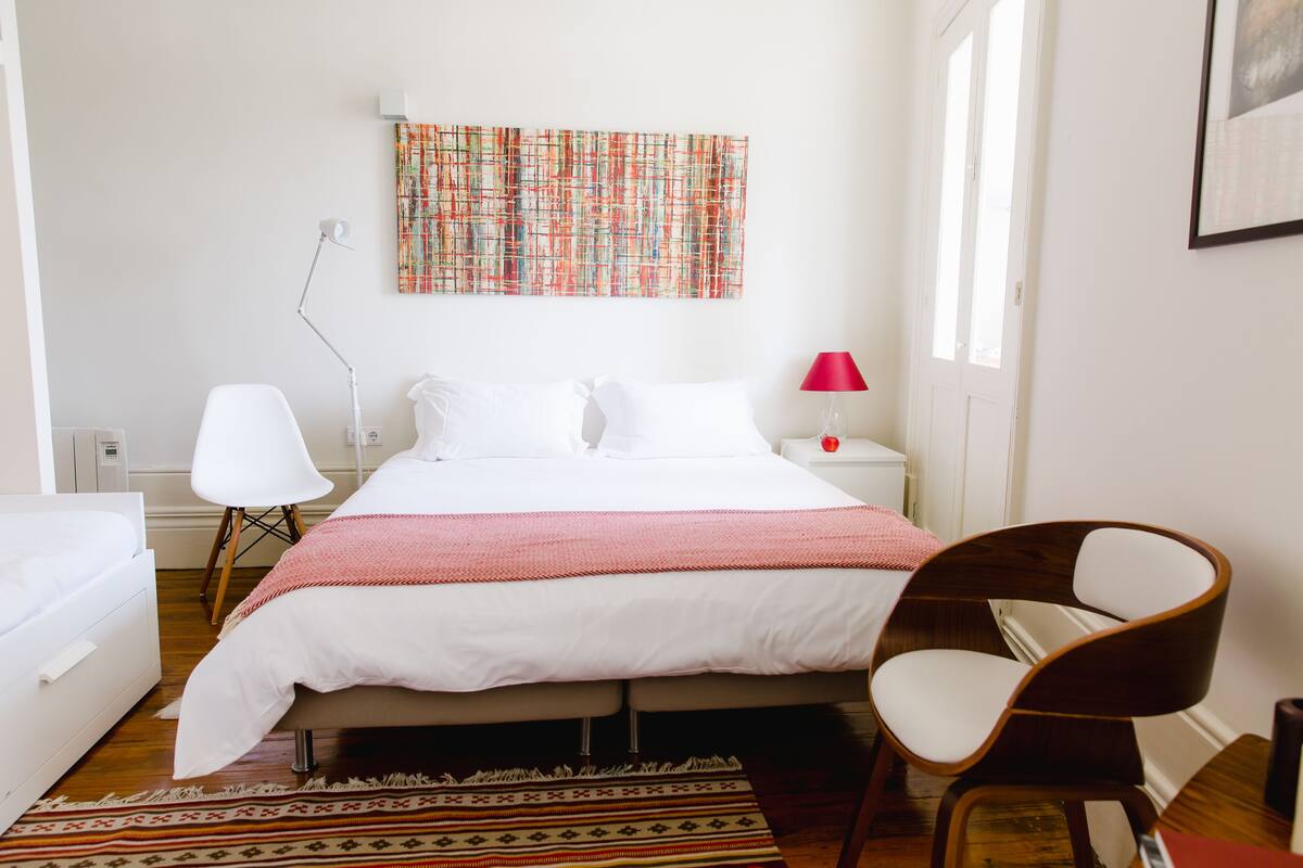 A bedroom with a bed, a desk, a chair, a lamp, and a window.