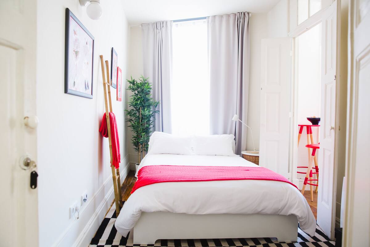 A narrow hotel room with a bed, a potted plant, and a red ladder.