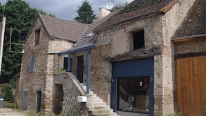 A stone building with a modern extension, featuring a staircase leading to a second floor, a large garage door, and a satellite dish on the roof.