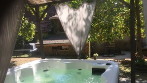 A hot tub in a covered outdoor area with a stone wall and a pergola.