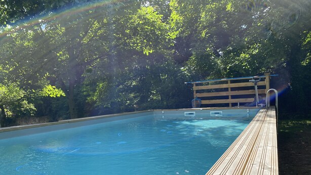 A swimming pool with a wooden deck, surrounded by trees.