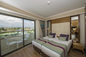 A hotel room with a large bed, a nightstand, a mirror, and a balcony with a view of the city. - Dream World Aqua Hotel - All Inclusive (Manavgat)