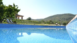 A clear blue swimming pool with tiled edges, surrounded by a grassy area and a hill in the background. - Agua Antigüa Casa Rural (Garguera)