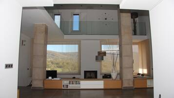Amplia sala de estar con techo alto, ventanas grandes y chimenea moderna.