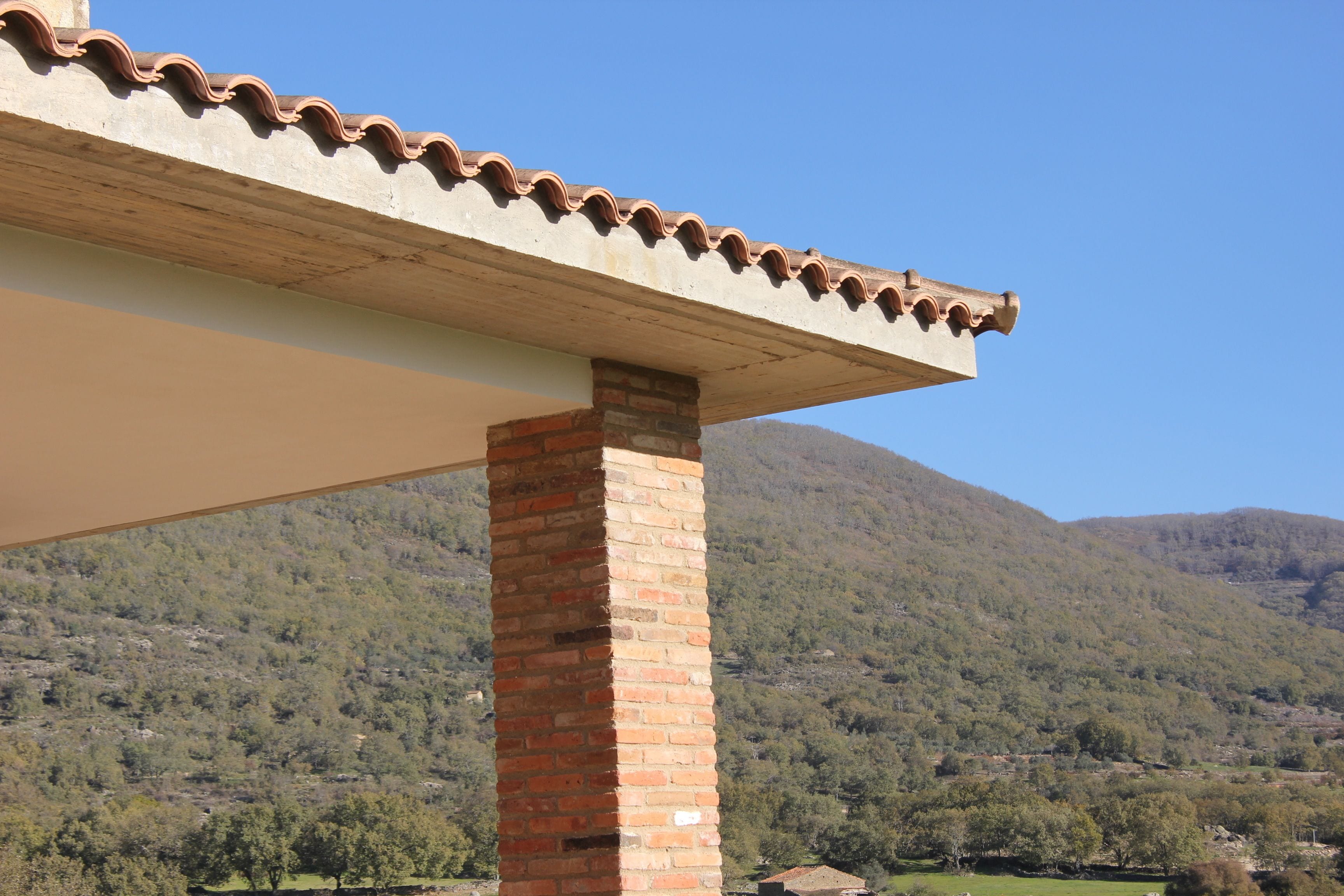 A brick column supporting a roof with a wavy edge, set against a mountainous backdrop.