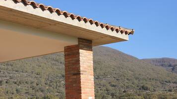 A brick column supporting a roof with a wavy edge, set against a mountainous backdrop.