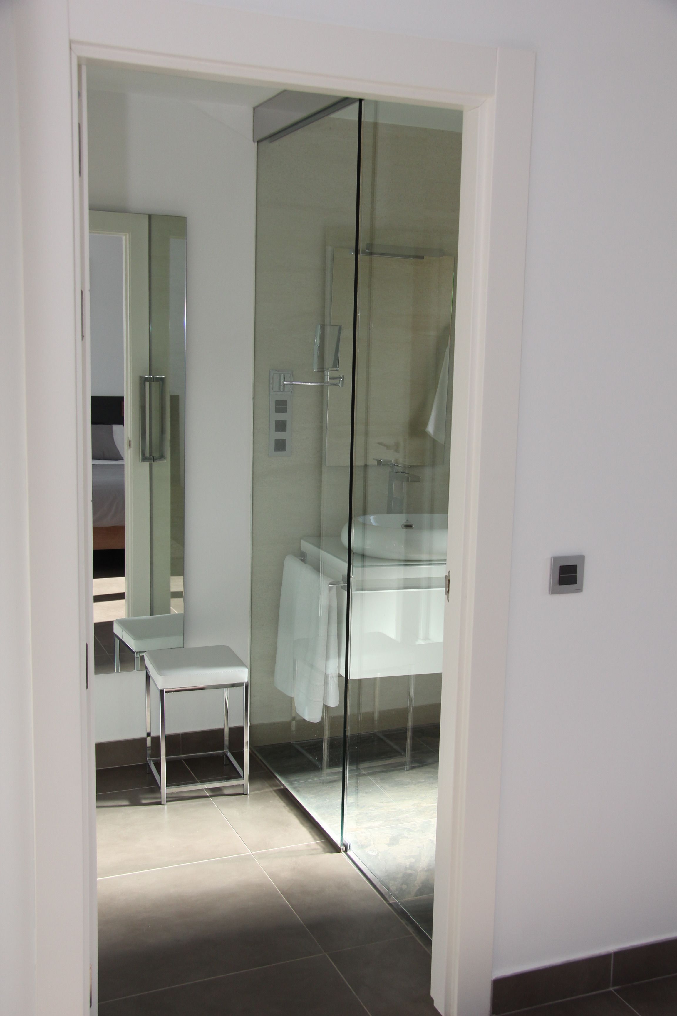 Un baño moderno con cabina de ducha de vidrio, un lavamanos blanco y un banco.
