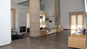 A spacious living area with a large central column, a long wooden bench, and a modern TV setup. - Agua Antigüa Casa Rural (Garguera)