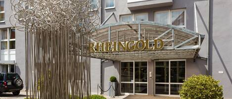 Entrada de hotel con una escultura moderna y un cartel que dice "RHEINGOLD".