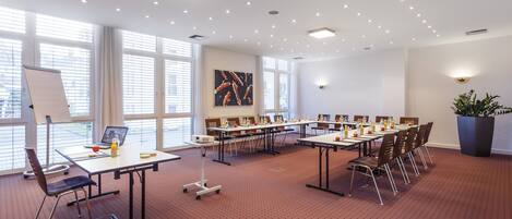 A conference room with multiple tables, chairs, a whiteboard, and a large window with blinds.