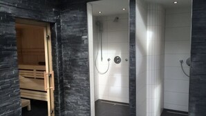 Un baño moderno con pared de piedra, un banco de madera y dos zonas de ducha separadas.