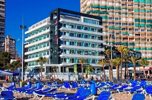 Un hotel con varios pisos, mobiliario exterior y palmeras.