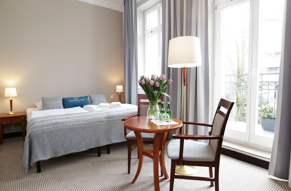 Una habitación de hotel con una cama, una mesa con sillas, una lámpara y un ventanal con cortinas.