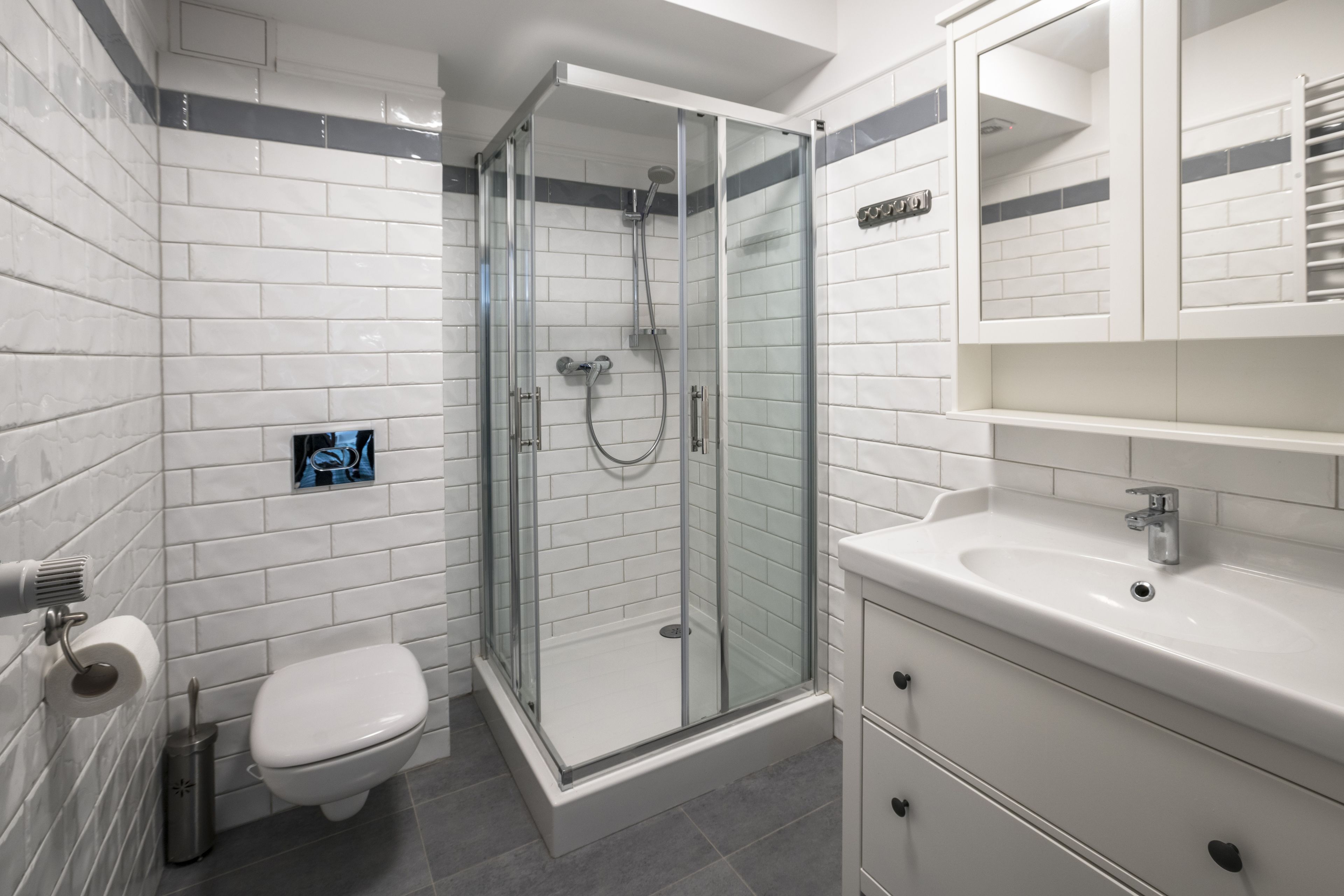 Un bagno moderno con piastrelle bianche tipo metro, una cabina doccia in vetro, un water bianco e un lavandino bianco con uno specchio sopra.