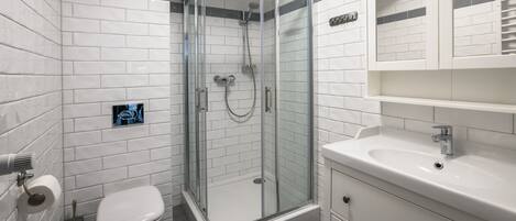 Un bagno moderno con piastrelle bianche tipo metro, una cabina doccia in vetro, un water bianco e un lavandino bianco con uno specchio sopra.