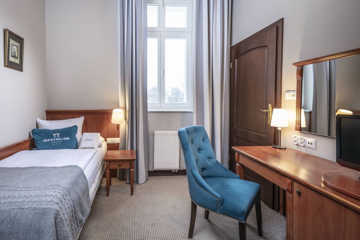A hotel room with a bed, a desk, a chair, a window, and a mirror.