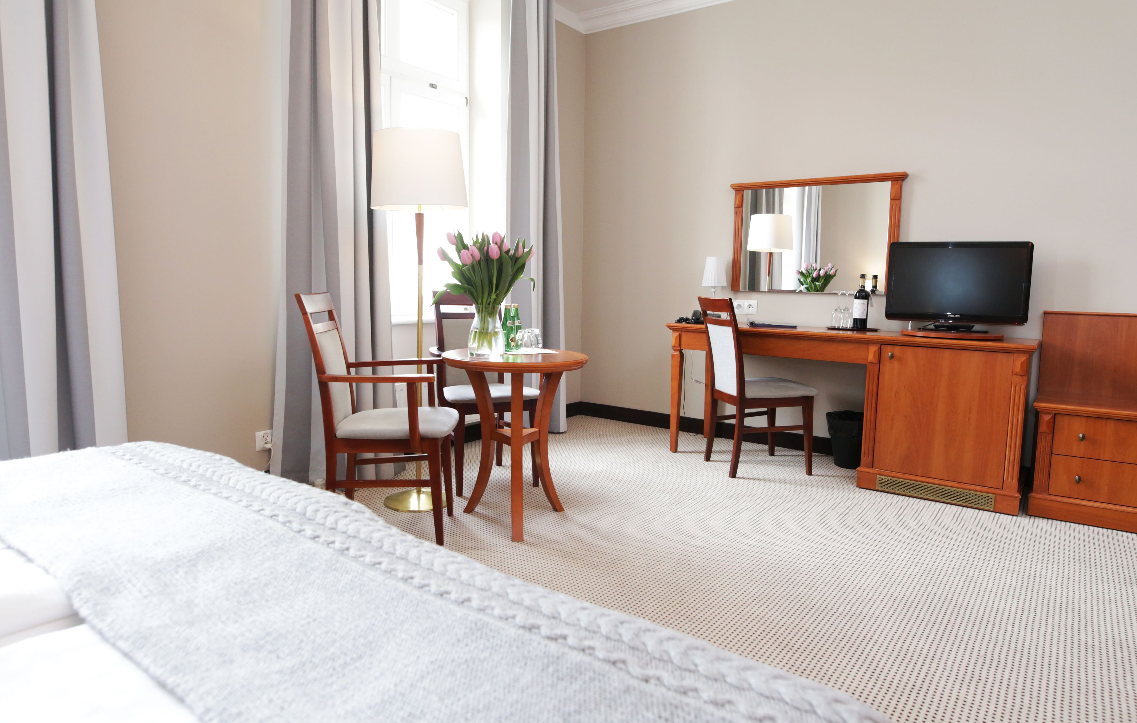 Une chambre d’hôtel comprenant un lit, un bureau, une chaise, une télévision et un vase avec des fleurs.