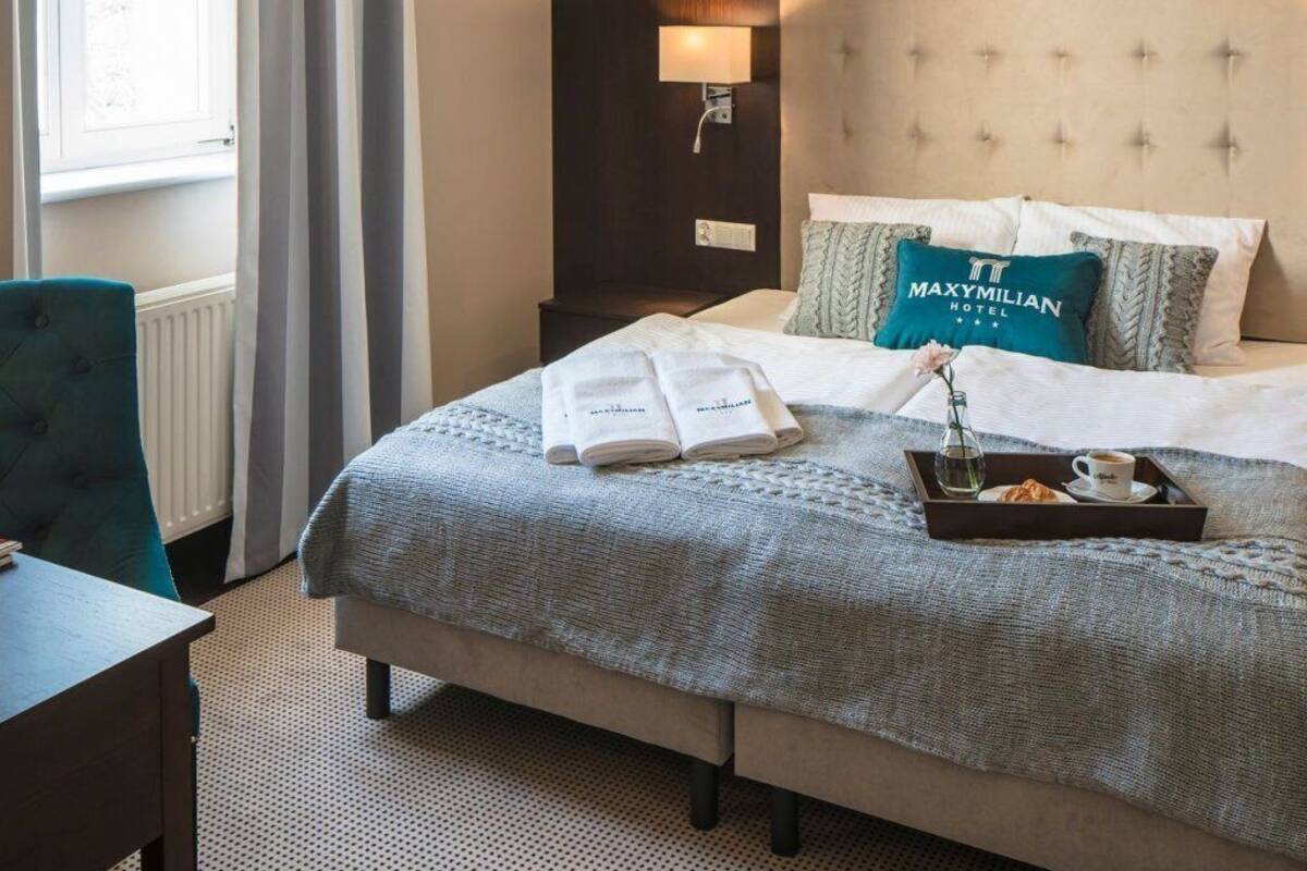 A hotel room with a bed, a nightstand, a lamp, a window with curtains, and a painting on the wall.