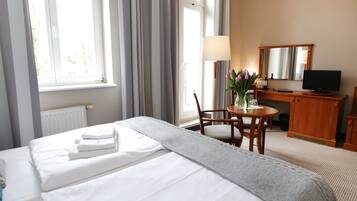 A hotel room with a bed, a desk, a chair, a lamp, a television, and a window with curtains.