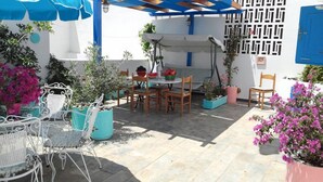 Eine Außenpatio mit einer Holz-Pergola, weißen Metallstühlen, einem Tisch und Kübelpflanzen.