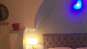 Ein Schlafzimmer mit einem Bett, einem Nachttisch mit Lampe, einer roten Schüssel und einer Wanduhr.