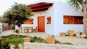 A white building with a wooden door and windows, a stone patio, and potted plants. - Gavdos Studios (Gavdos)