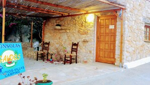 Un bâtiment en pierre avec une porte en bois, deux chaises en bois, une petite table et une enseigne.