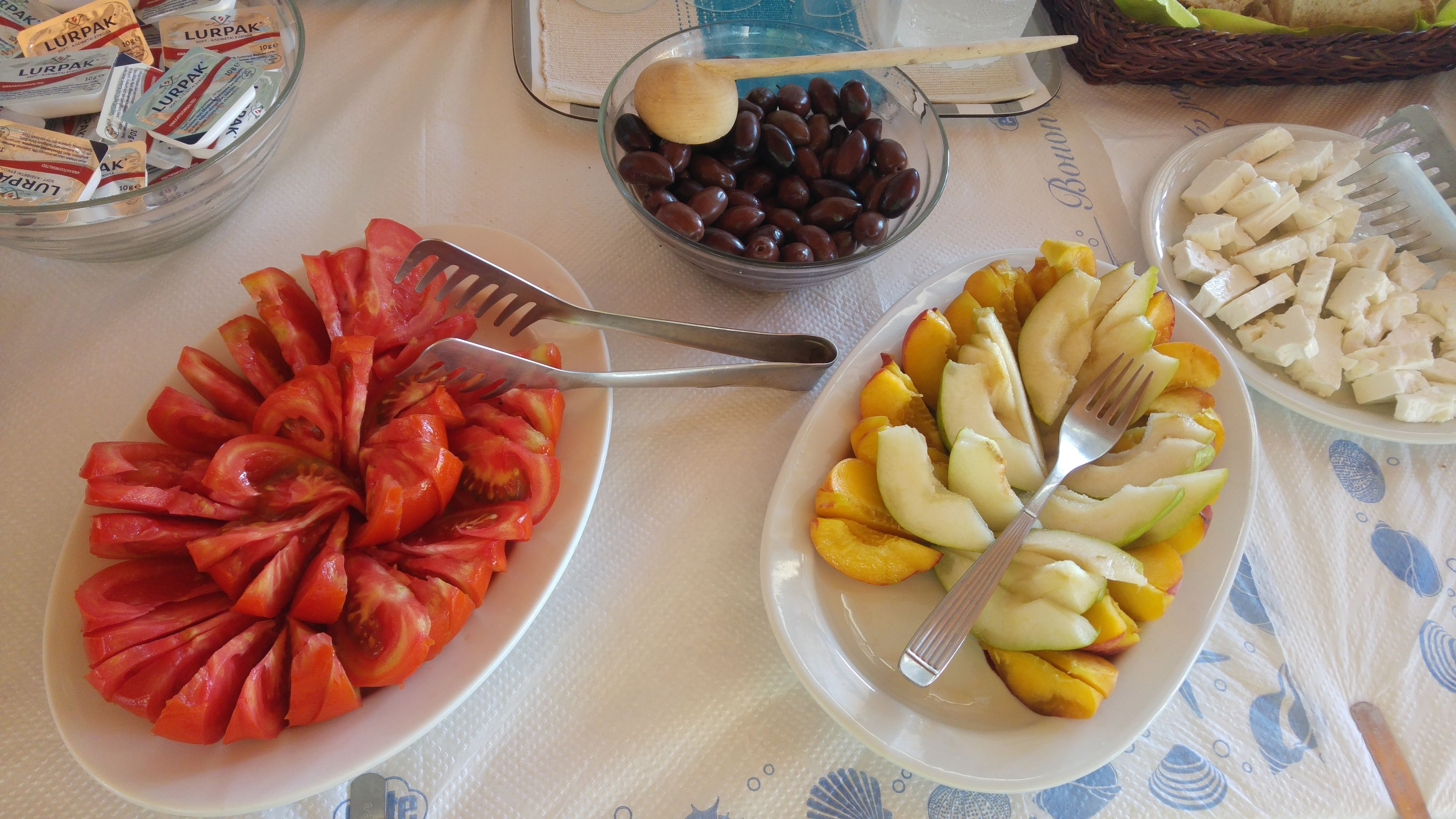 Una mesa con platos de tomates en rodajas, aceitunas y frutas.