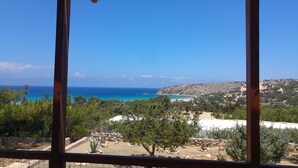 Une vue sur la côte, aperçue à travers une fenêtre, avec un ciel dégagé, une plage de sable et une colline rocheuse.