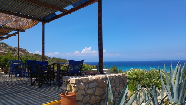 Une terrasse avec des murs en pierre, des chaises bleues et une vue sur la mer.