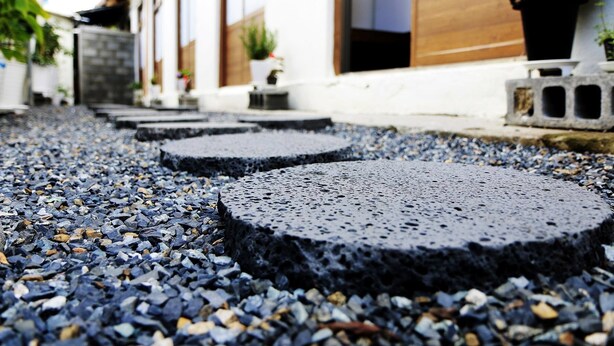 A pathway with circular stepping stones made of dark material, leading through a residential area with white buildings and potted plants. - Dodam Guest House (Busan)