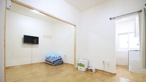 A room with a wooden floor, a flat-screen TV mounted on the wall, a small white cabinet, and a door leading to another room. - Dodam Guest House (Busan)