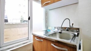 A small kitchen with a window, a sink, and wooden cabinets. - Dodam Guest House (Busan)