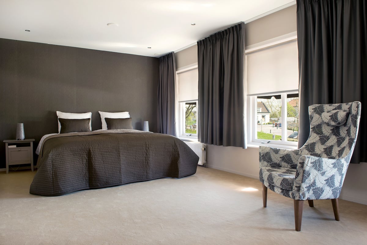 A bedroom with a large bed, a chair, a nightstand, and a window with curtains.