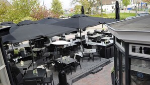 Un patio al aire libre con varias mesas y sillas, cubierto por grandes sombrillas.