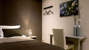 Habitación de hotel con cama, mesita de noche, silla, escritorio y un cuadro en la pared.