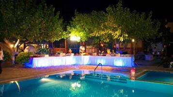 An outdoor pool area with a covered seating area and trees in the background.