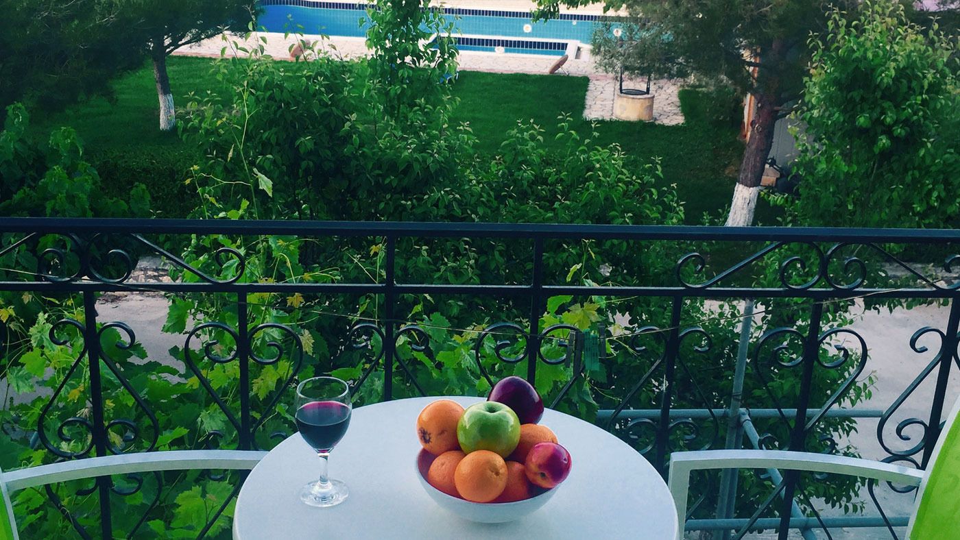 A balcony with a table, a bowl of fruit, and a glass of red wine.