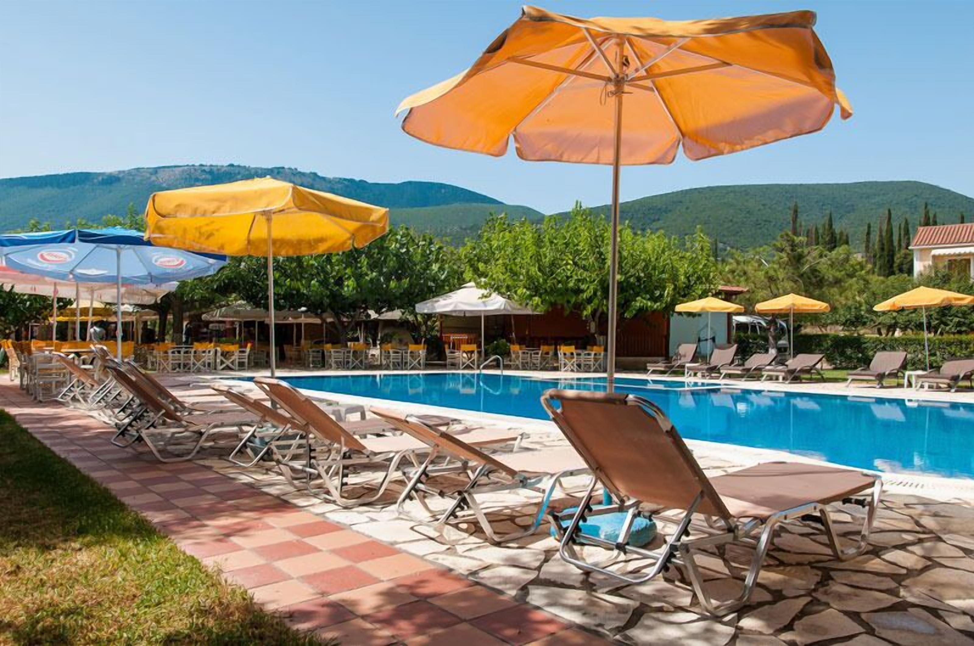A poolside area with lounge chairs and umbrellas, a clear sky, and a mountainous backdrop.