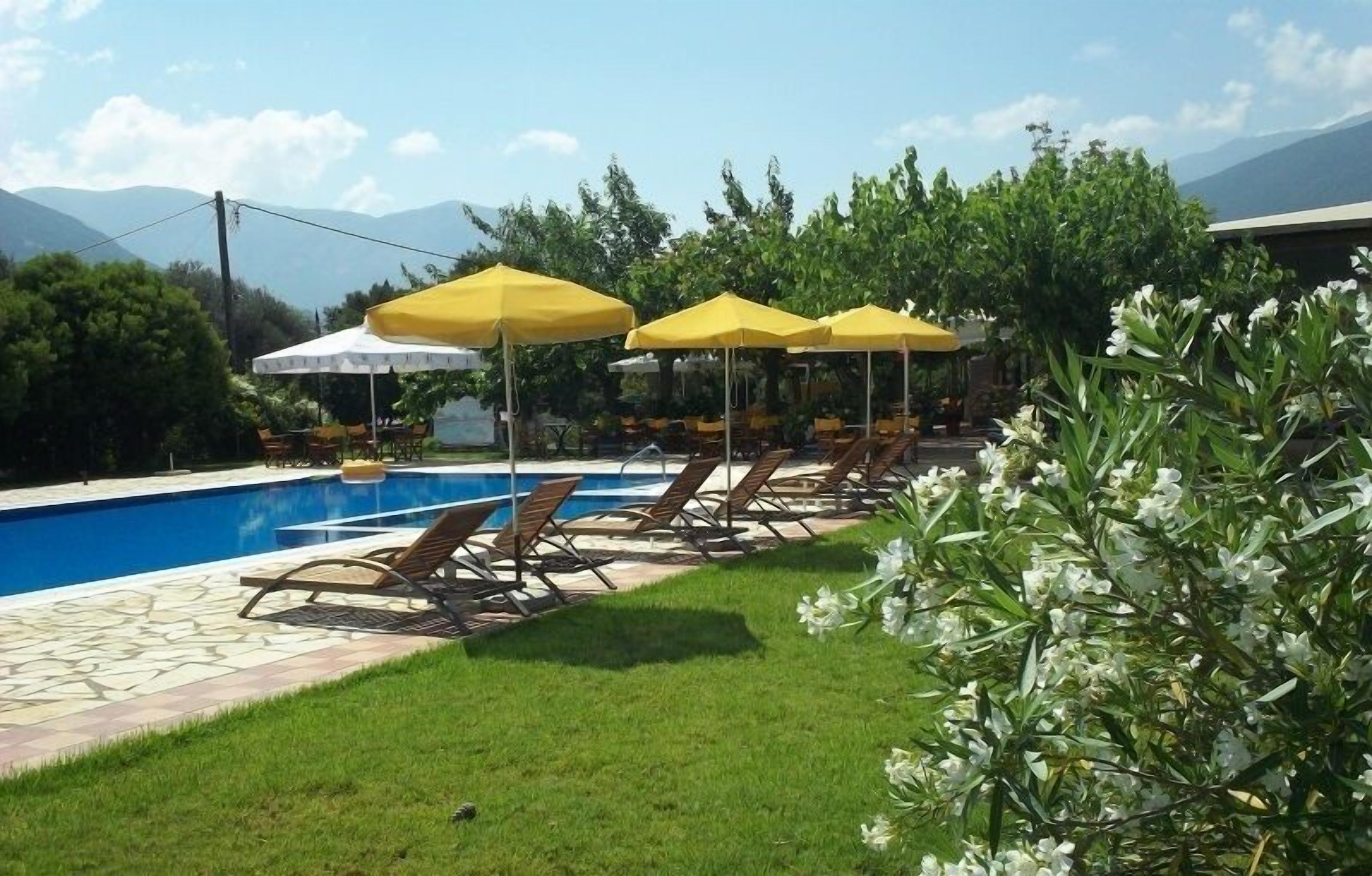A poolside area with lounge chairs and yellow umbrellas, surrounded by greenery and mountains in the background.