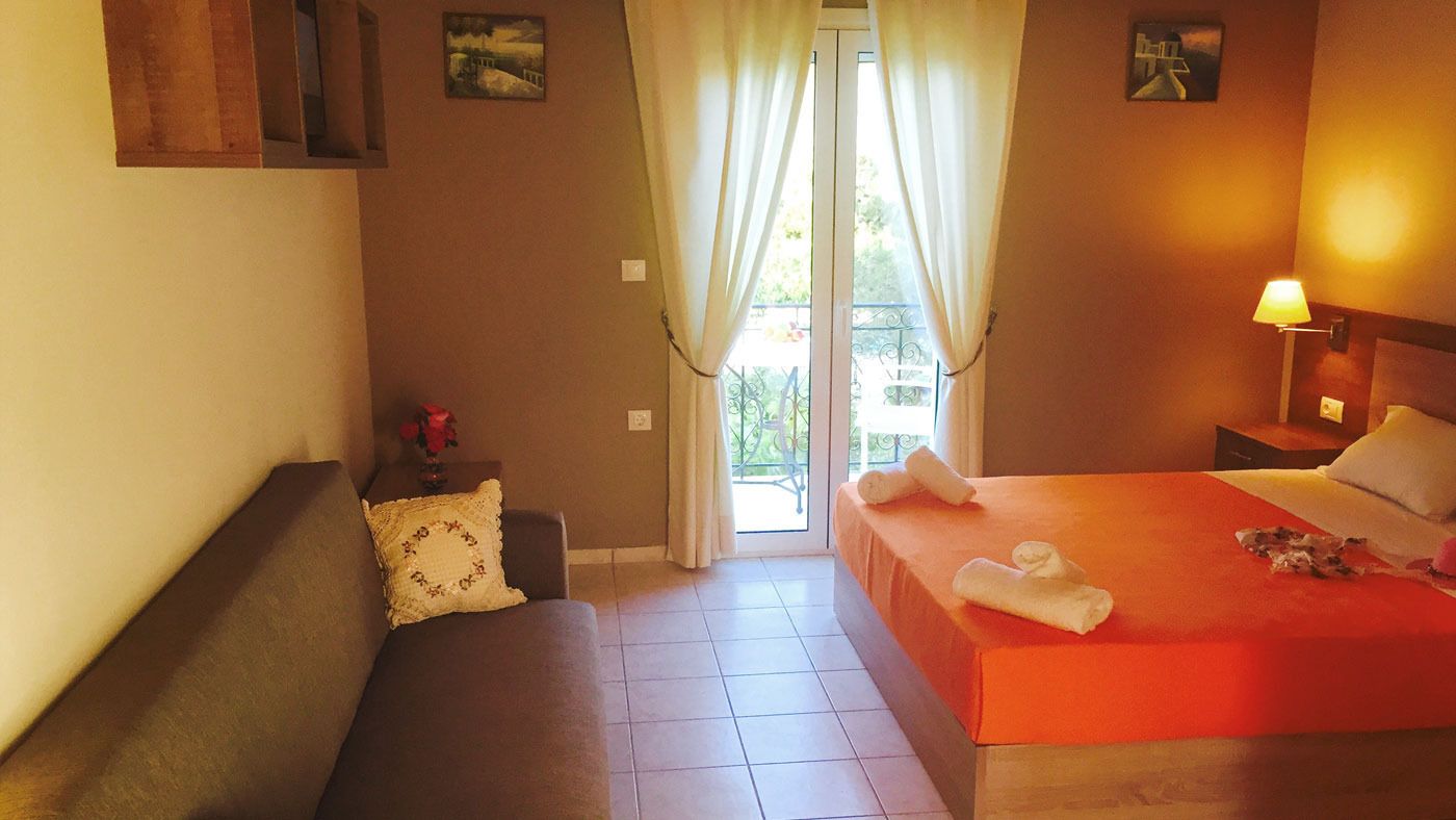 A hotel room with a bed, a sofa, a window with curtains, and a balcony.